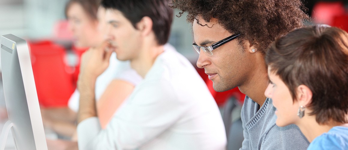 Group of people working on computers in a classroom or office setting.